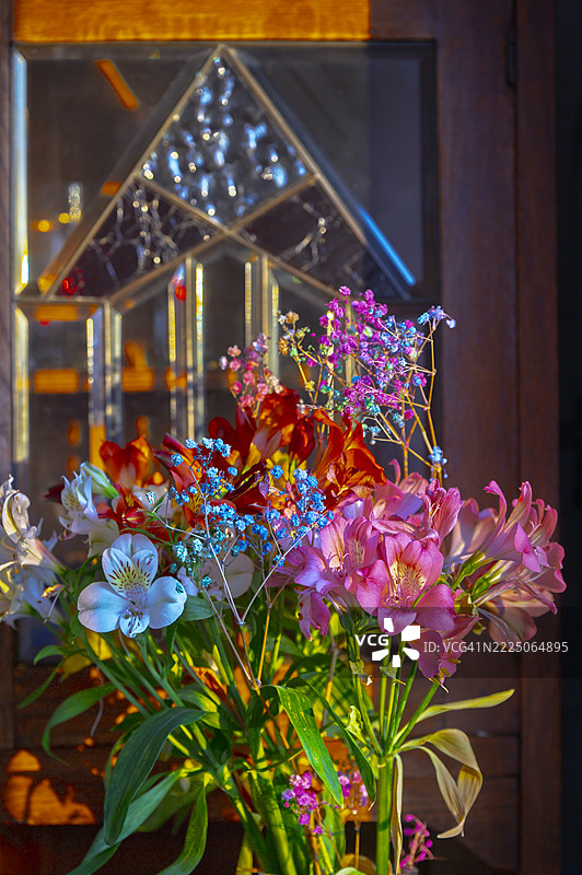 五彩缤纷的花朵在彩色玻璃窗透出的夕阳光辉下绽放图片素材