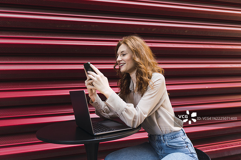 美丽的女人坐在城市波纹铁附近使用智能手机图片素材