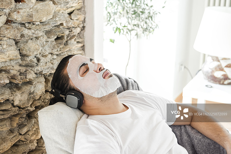 Man relaxing with a face mask and headphones in a living room图片素材