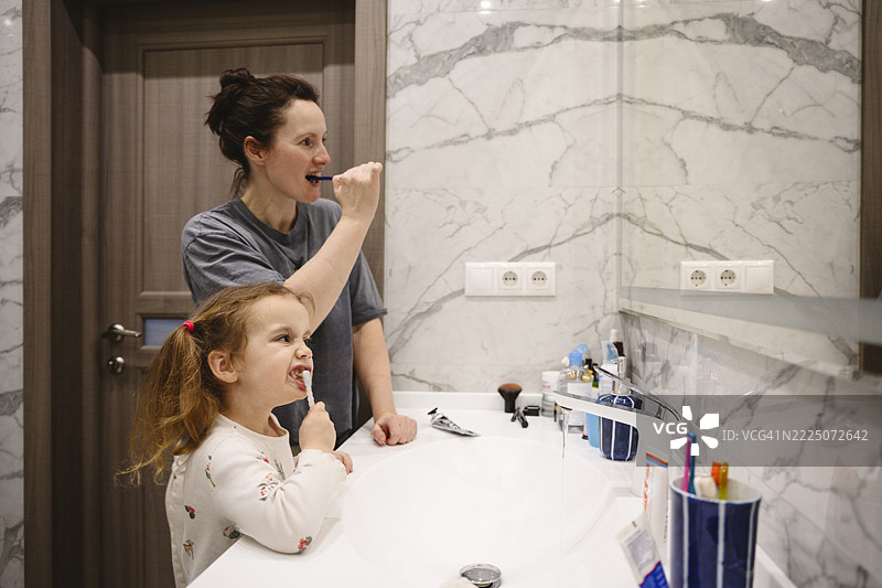 Mother and daughter brushing teeth together in the bathroom图片素材