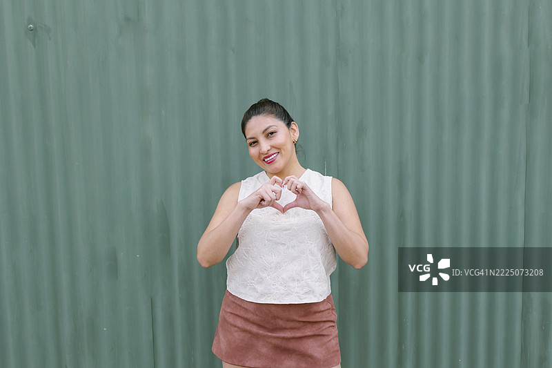 Woman making a heart gesture with her hands against a green background图片素材