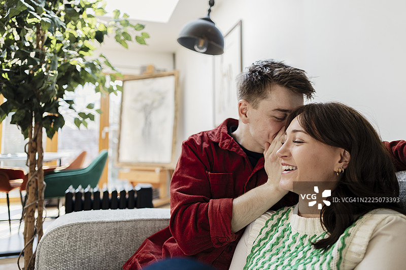 A couple sharing a secret and laughing together at home图片素材