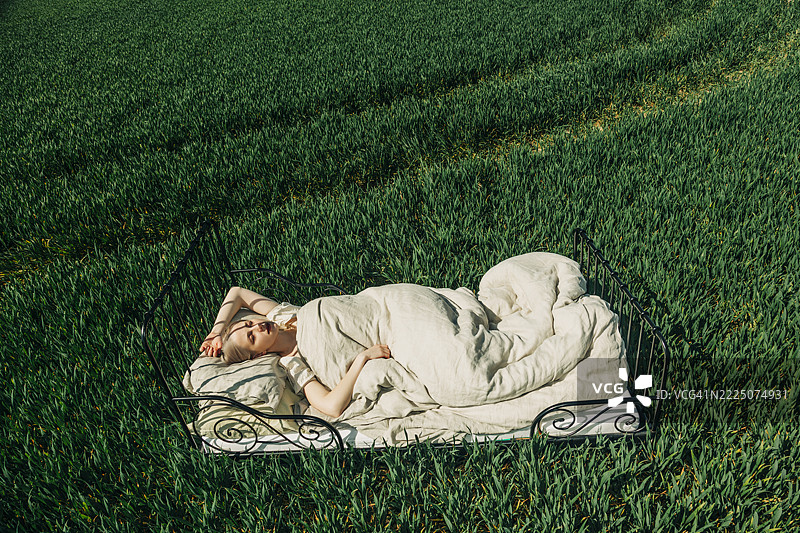 Woman sleeping on a bed in a green field under the open sky图片素材