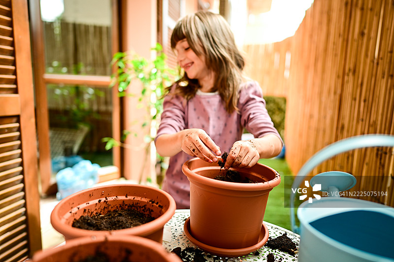 微笑的女孩在阳台上园艺，正在陶土花盆里种植种子图片素材
