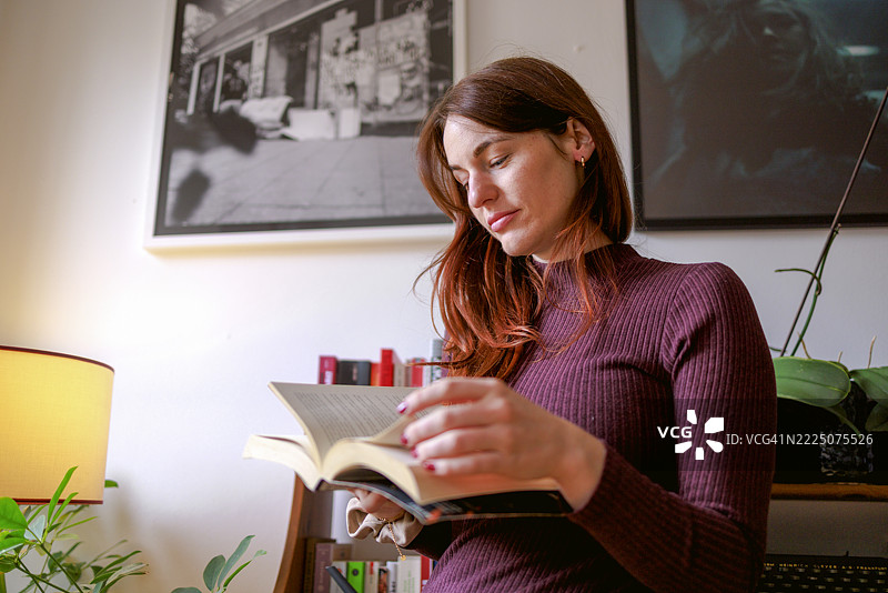 Brunette woman reading a book in a cozy home office setting图片素材