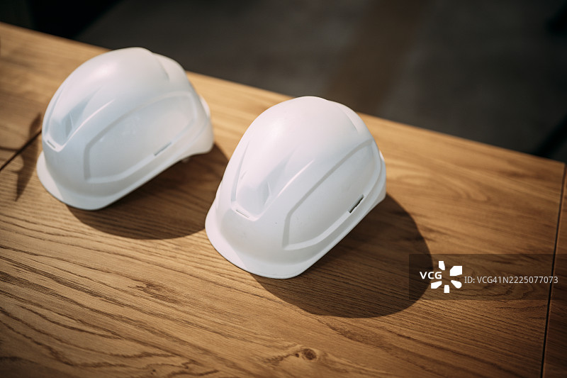两顶白色安全帽放在室内的木桌上，象征着工程中的安全与团队合作。图片素材
