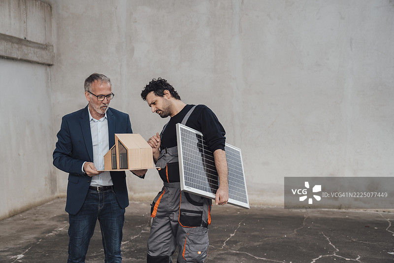 Engineer and colleague discussing a model and solar panel outdoors图片素材