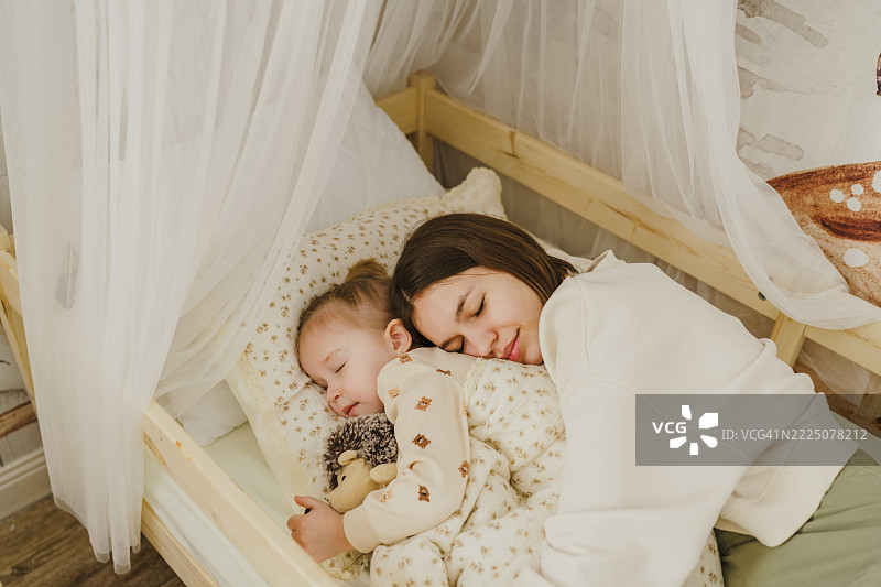 母亲在温馨的儿童房里拥抱女儿，准备入睡。图片素材