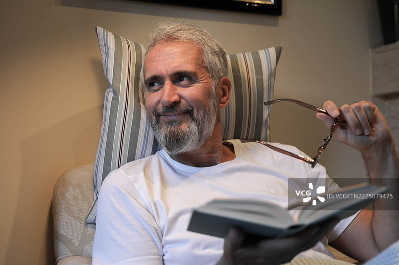 放松的老年男子在家中阅读一本书图片素材