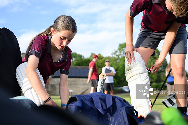 年轻的少女正在穿戴护具，准备与板球队练习击球。图片素材