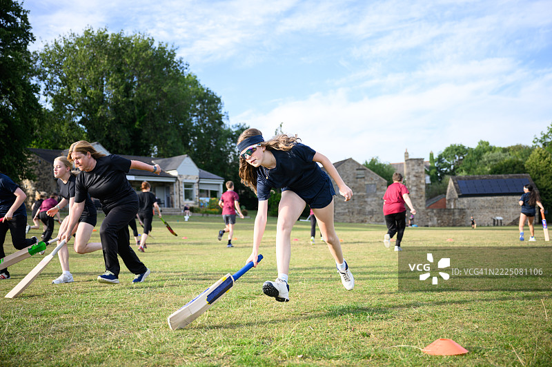 青少年女孩在一群不同年龄的女性和女孩中练习滑行板球。图片素材