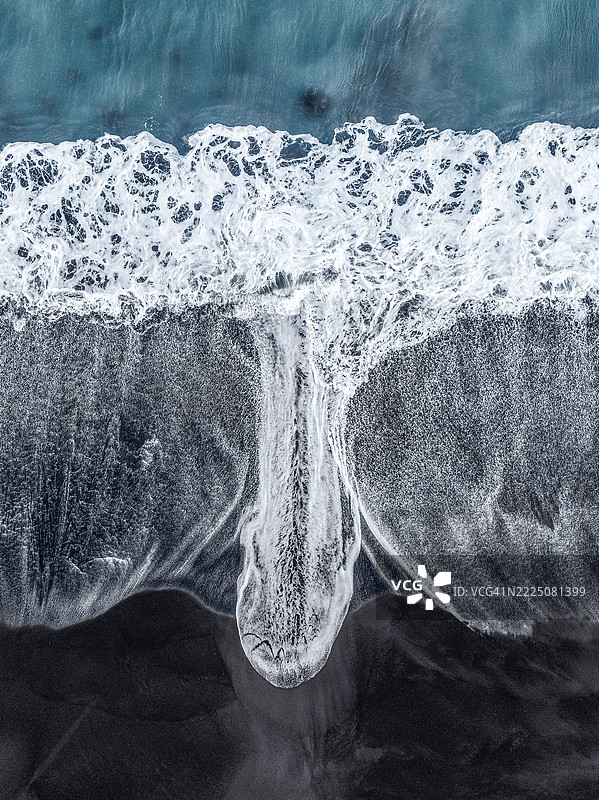 无人机拍摄的图像，展示了一道延伸的海浪冲击巴厘岛克伦贡区的黑沙滩。图片素材