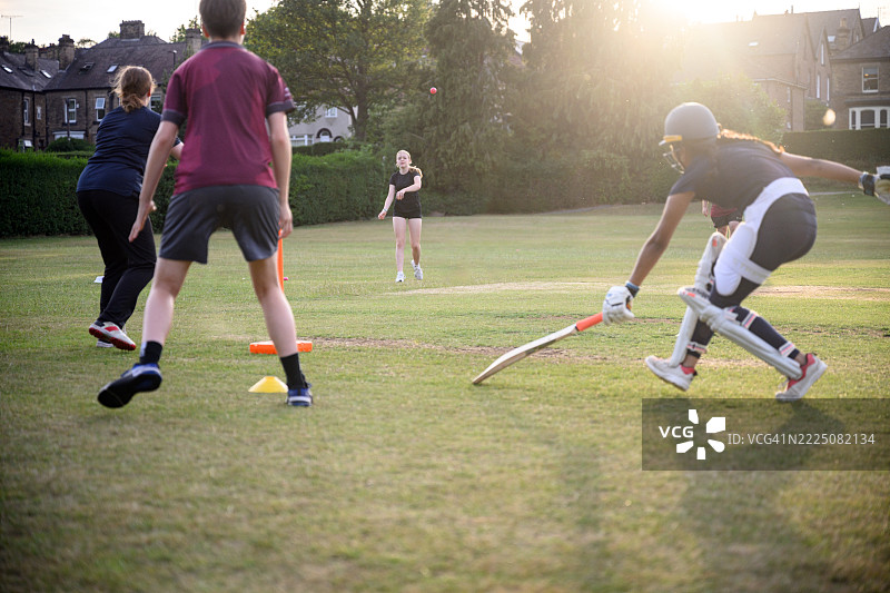 击球手在球场上滑动球棒，场上队员将球扔回门柱。图片素材