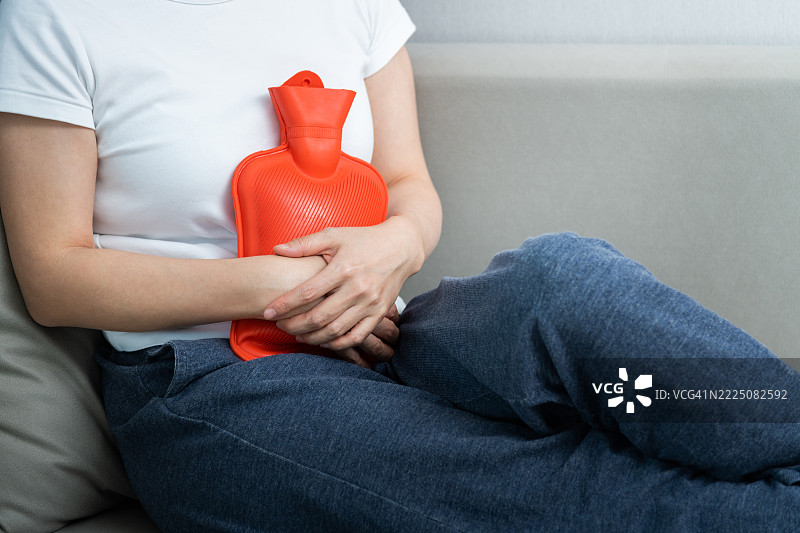 女人坐在沙发上抱着一个橙色的热水袋图片素材