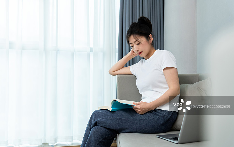 女人坐在沙发上阅读一本书图片素材
