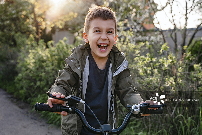 男孩在夏天的街道上骑自行车，面带微笑，玩得很开心图片素材