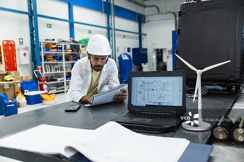 工程师在车间使用笔记本电脑和风力涡轮机模型审查蓝图图片素材