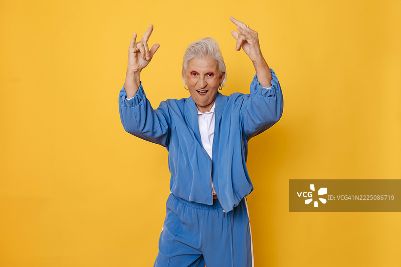 活力四射的老年女性穿着蓝色运动服，摆姿势于黄色背景前图片素材