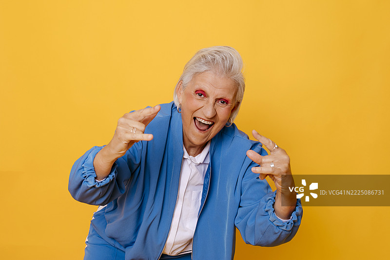 穿着蓝色夹克的快乐老年女性在黄色背景前摆姿势图片素材