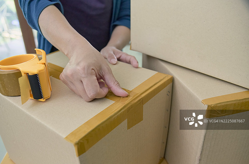女性近距离拍摄正在用胶带封箱纸盒以便运输和递送图片素材