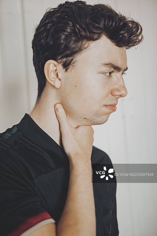 年轻男子面露痛苦表情，手触喉咙，表示不适或喉咙痛图片素材