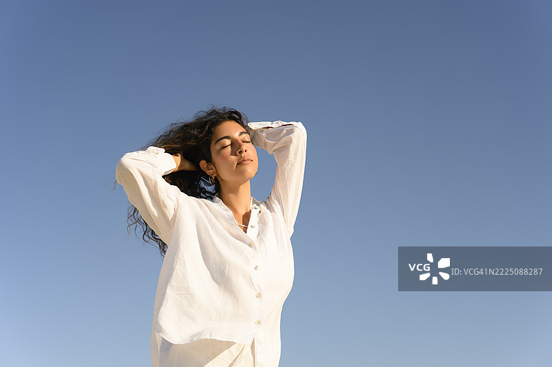 女人在晴朗的蓝天下享受宁静的户外时光图片素材