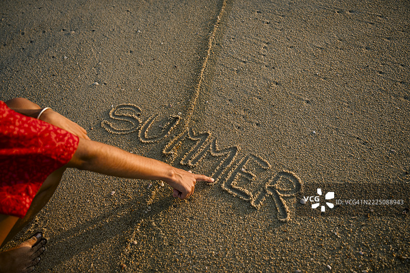 一个无法辨认的人在海滩的沙子上写下“夏天”图片素材