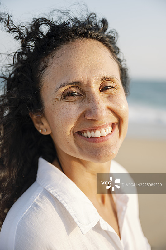 阳光下穿着白衬衫的女人在海滩上微笑图片素材