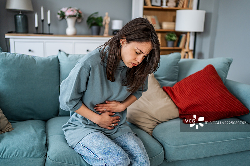 年轻女性坐在沙发上，感到腹部疼痛图片素材