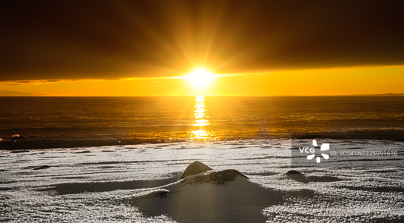 被厚厚云层笼罩的雪覆盖海滩，星星般的阳光透出。图片素材