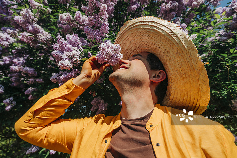 戴着草帽和黄色衬衫的男人在乡村环境中闻紫色丁香花图片素材