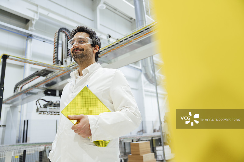 工厂里的工程师戴着安全眼镜和白大褂，手里拿着一款新产品。图片素材