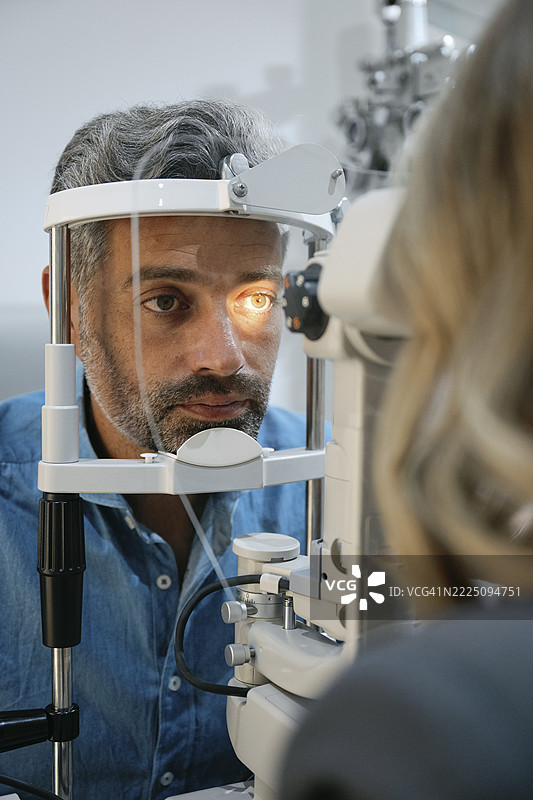男子在诊所接受眼部检查，明亮的灯光照射着他的眼睛图片素材