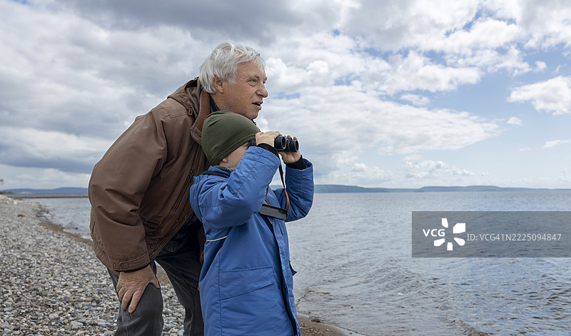祖父和孙子在阴天用望远镜探索海滩图片素材