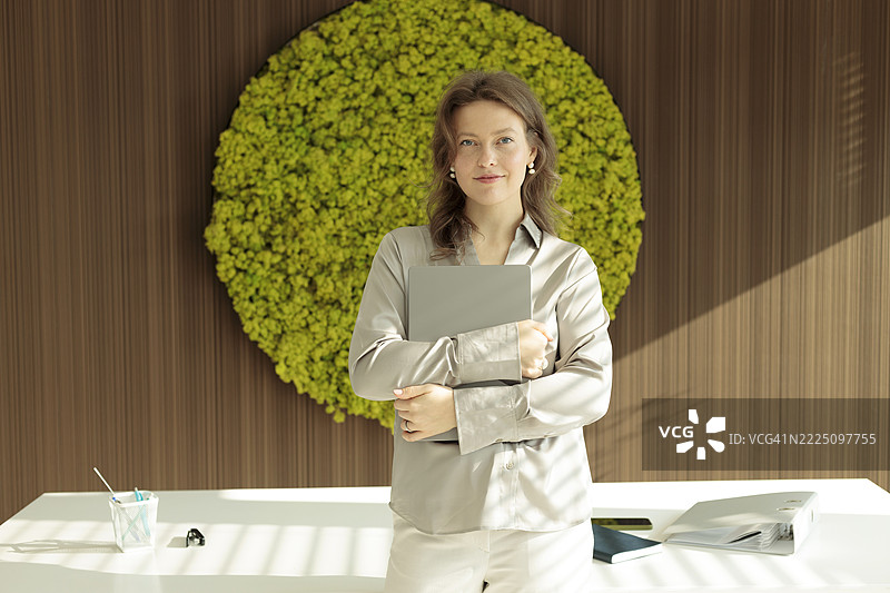 现代办公室中微笑的女商人肖像，背景是一面绿色墙壁图片素材