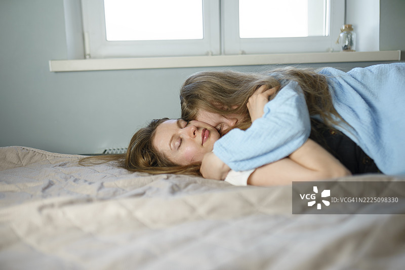 母女在室内床上拥抱，展现亲情与团结。图片素材