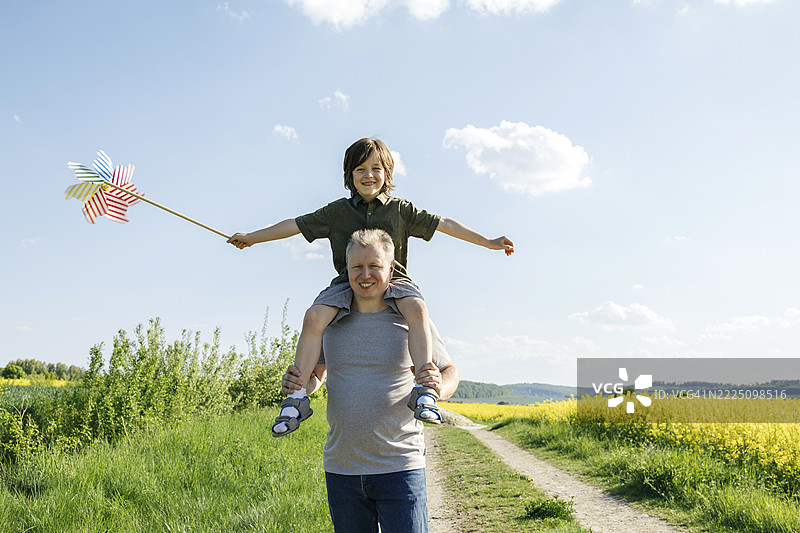 父亲在夏天户外背着儿子，手里拿着风车图片素材