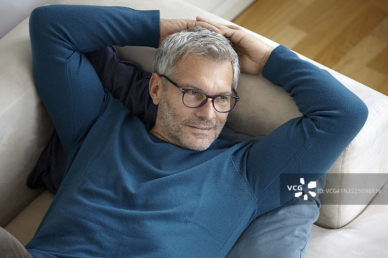 男人在家中沙发上放松，戴着眼镜，穿着蓝色毛衣。图片素材