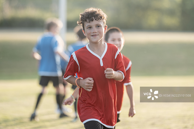 孩子们在阳光明媚的日子里穿着红色和蓝色球衣在户外踢足球图片素材