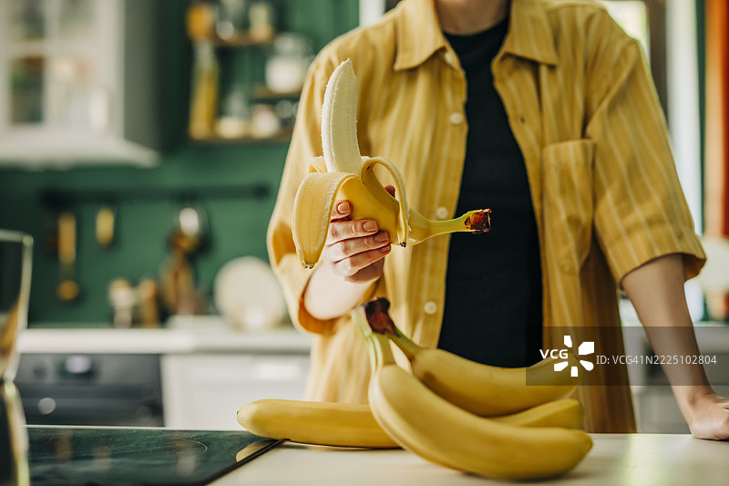 中年男性穿着黄色衬衫在厨房里剥香蕉图片素材