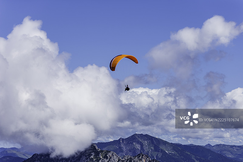 在阳光明媚的日子里，五彩斑斓的滑翔伞在云层中飞翔，俯瞰群山。图片素材