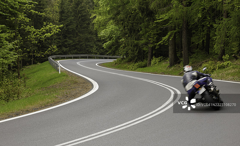 摩托车手在春季的郁郁葱葱的森林中穿行于蜿蜒的道路上图片素材