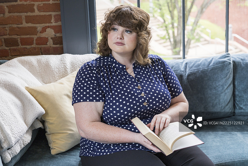 一位残疾女性在家中放松，坐在沙发上阅读一本书。图片素材