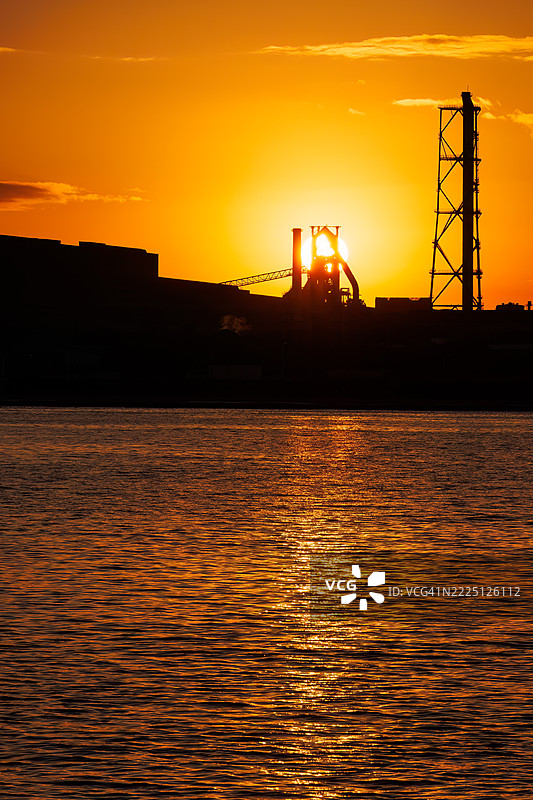 第一缕阳光升起，照耀着运河对岸的烟囱和电厂、钢铁厂的植物。图片素材
