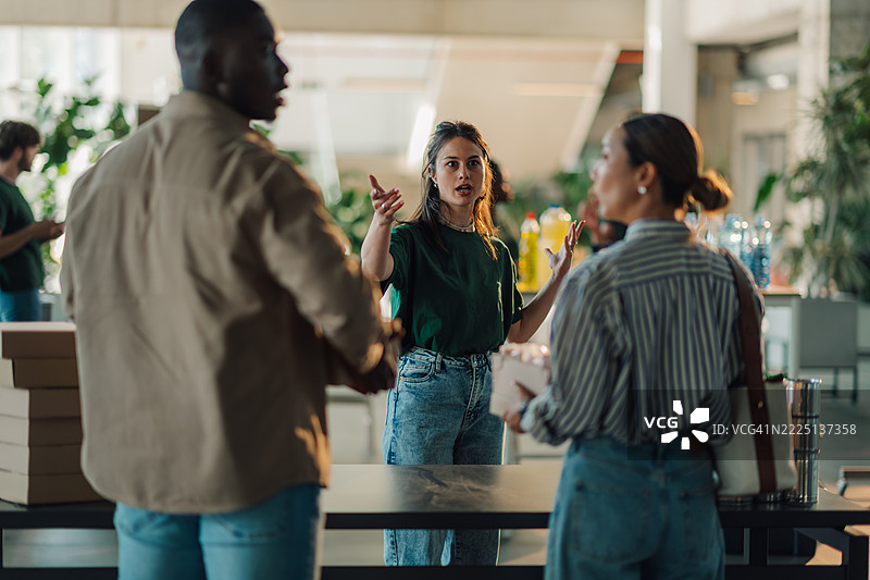 年轻女性在团队会议上主导讨论，同时手里拿着一个披萨盒图片素材