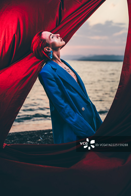 一位身穿西装外套的女士拉开窗帘，欣赏着海面上生机勃勃的日落景色。图片素材