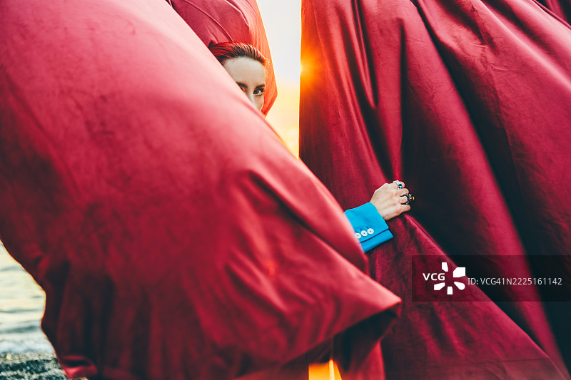 一位身穿西装外套的女士拉开窗帘，欣赏着海上绚烂的日落。图片素材