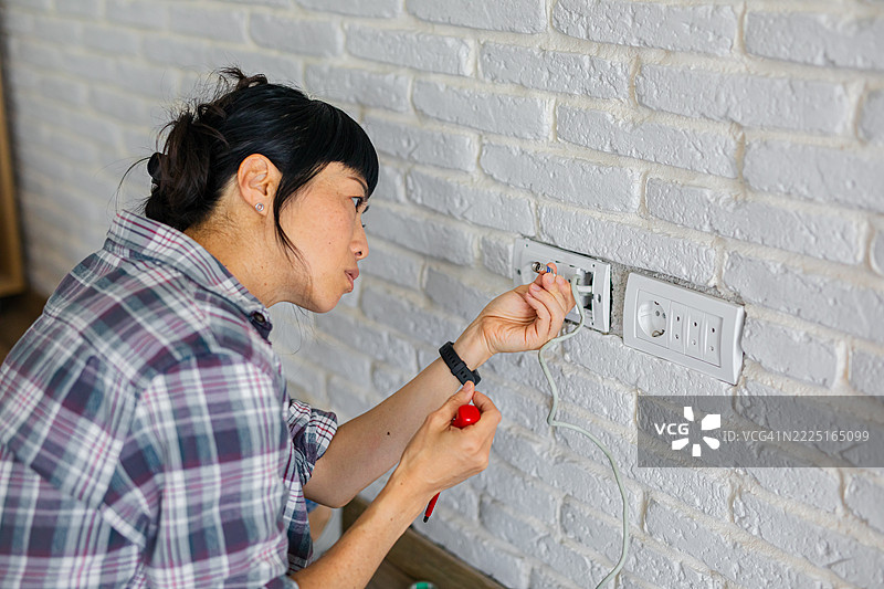 专注的女电工坐在地板上进行现代家居的DIY墙壁插座安装图片素材