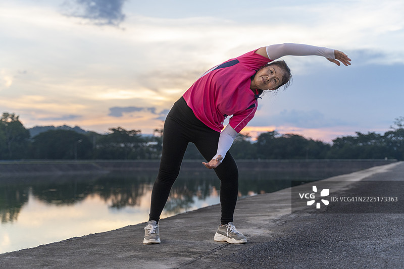 穿着粉色运动服的亚洲老年女性在户外拉伸图片素材