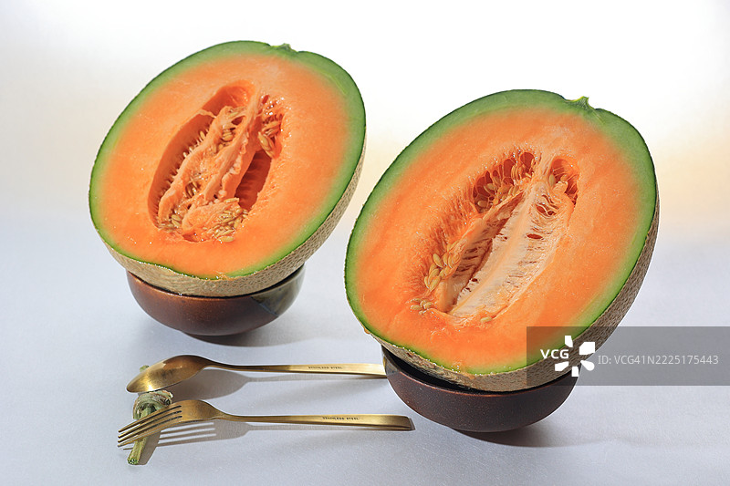 甜美多汁的北海道哈密瓜，完美对半切开，随时可以享用。体验优质日本夏季的奢华——味道浓郁，色彩鲜艳，搭配金色餐具呈现得美轮美奂。图片素材